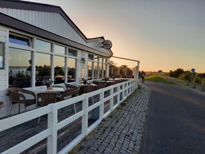 Un restaurante con terraza, una cerca blanca y un sendero pavimentado.