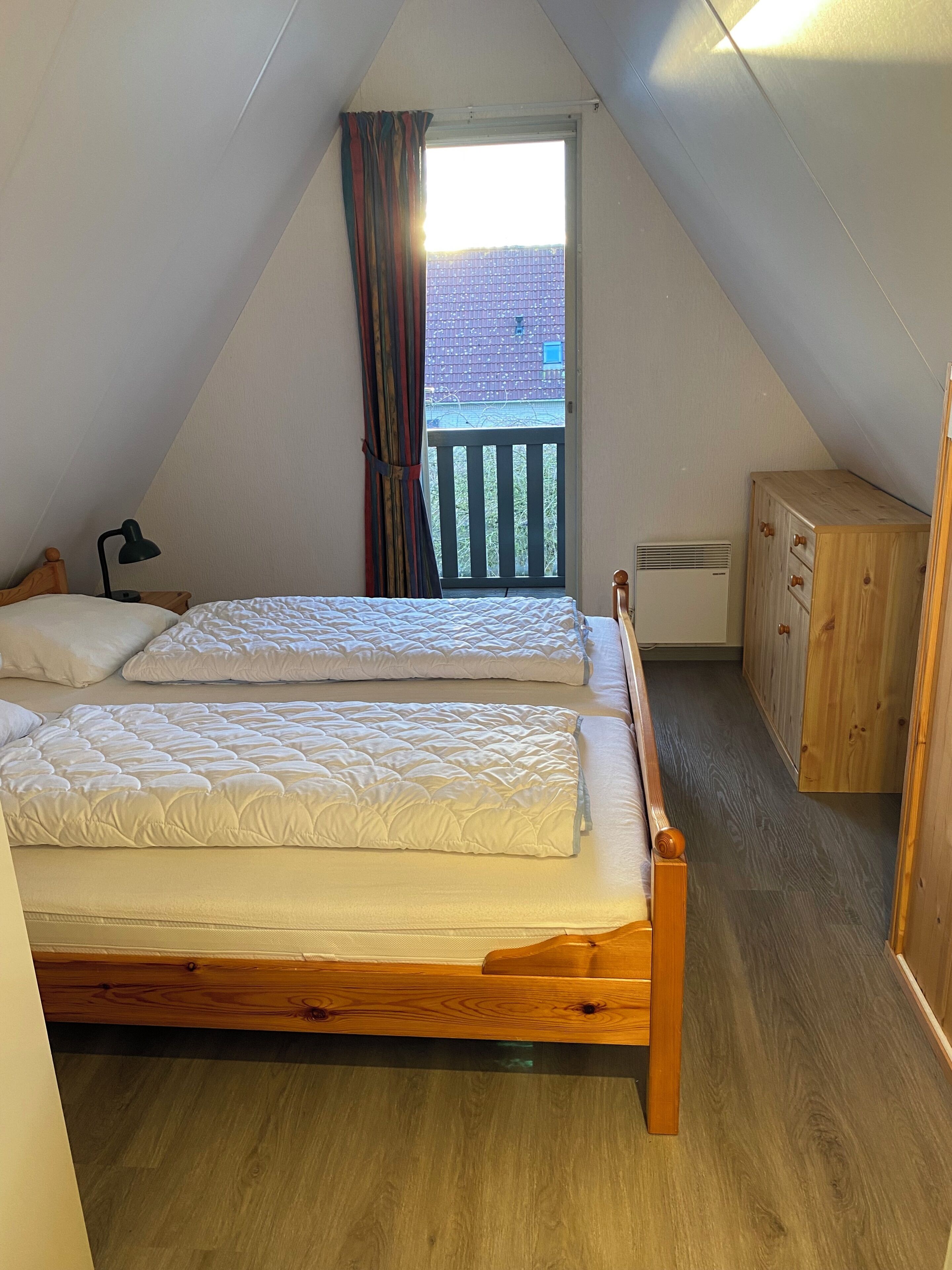 A bedroom with two beds, a wooden wardrobe, and a view of a balcony.