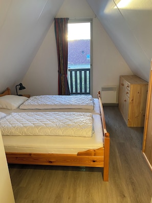 A bedroom with two beds, a wooden wardrobe, and a view of a balcony.