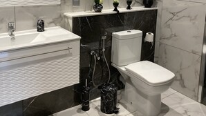 A modern bathroom with a white sink, black marble accents, a toilet, and a mirror with a unique wavy design.