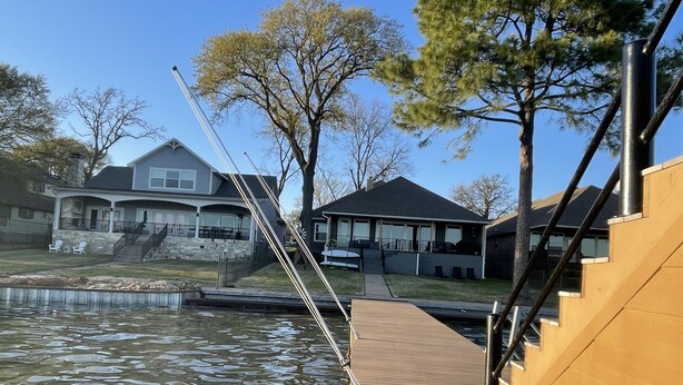 A wooden dock extending over a body of water with houses in the background. - McDonald Manor at Cedar Creek Lake| Modern Lakefront Getaway (Gun Barrel City)