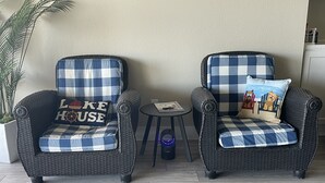Two wicker armchairs with checkered cushions, a small round table, and a potted plant. - McDonald Manor at Cedar Creek Lake| Modern Lakefront Getaway (Gun Barrel City)