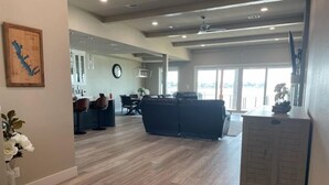 A spacious living area with a large dark-colored sofa, a dining table with chairs, and a kitchen area with a refrigerator. - McDonald Manor at Cedar Creek Lake| Modern Lakefront Getaway (Gun Barrel City)