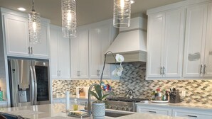 A modern kitchen with white cabinets, a large island with bar stools, a gas stove, and pendant lighting. - McDonald Manor at Cedar Creek Lake| Modern Lakefront Getaway (Gun Barrel City)