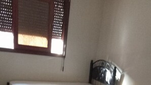 A small, single-bed room with a tiled floor and a window with blinds.