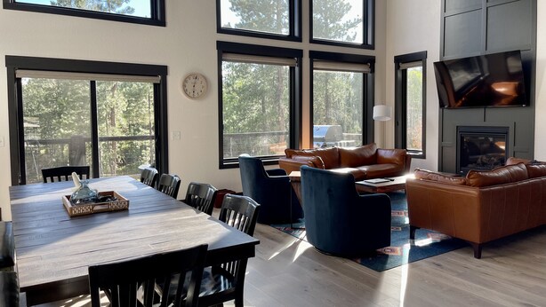 Un vaste espace de vie comprenant une grande table en bois, plusieurs chaises, un canapé bleu et un divan en cuir. On y trouve également une cheminée et un téléviseur fixé au mur.