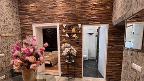 Un intérieur moderne avec un mur en pierre, une table en verre ornée d’un vase de fleurs et une vue sur une salle de bain.