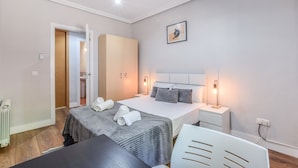 Habitación de hotel con cama, mesitas de noche, una silla, un radiador y una puerta que da a otra habitación.