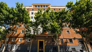Un edificio de varios pisos con entrada central, balcones y árboles en la fachada.