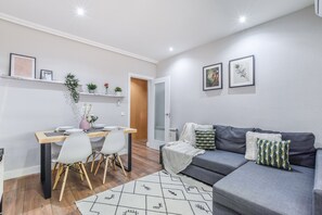 A modern living room with a grey sofa, a dining table with chairs, and a small kitchen area. - Spacious Comfort in the Heart of Madrid (Madrid)