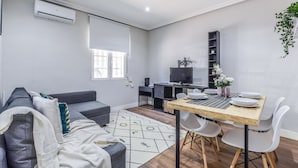 Una sala de estar moderna con un sofá gris, una mesa de comedor con sillas, un televisor y una estantería.