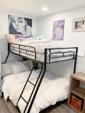 Een slaapkamer met een stapelbed, een onderbed, een ladder en een klein houten plankje.