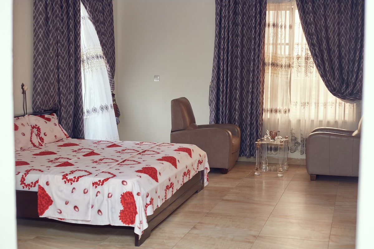 Ein Schlafzimmer mit einem Bett, zwei Stühlen, einem kleinen Tisch und Vorhängen.