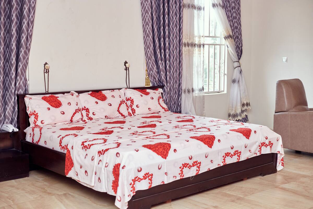 Een slaapkamer met een bed, gordijnen, een stoel en een raam.