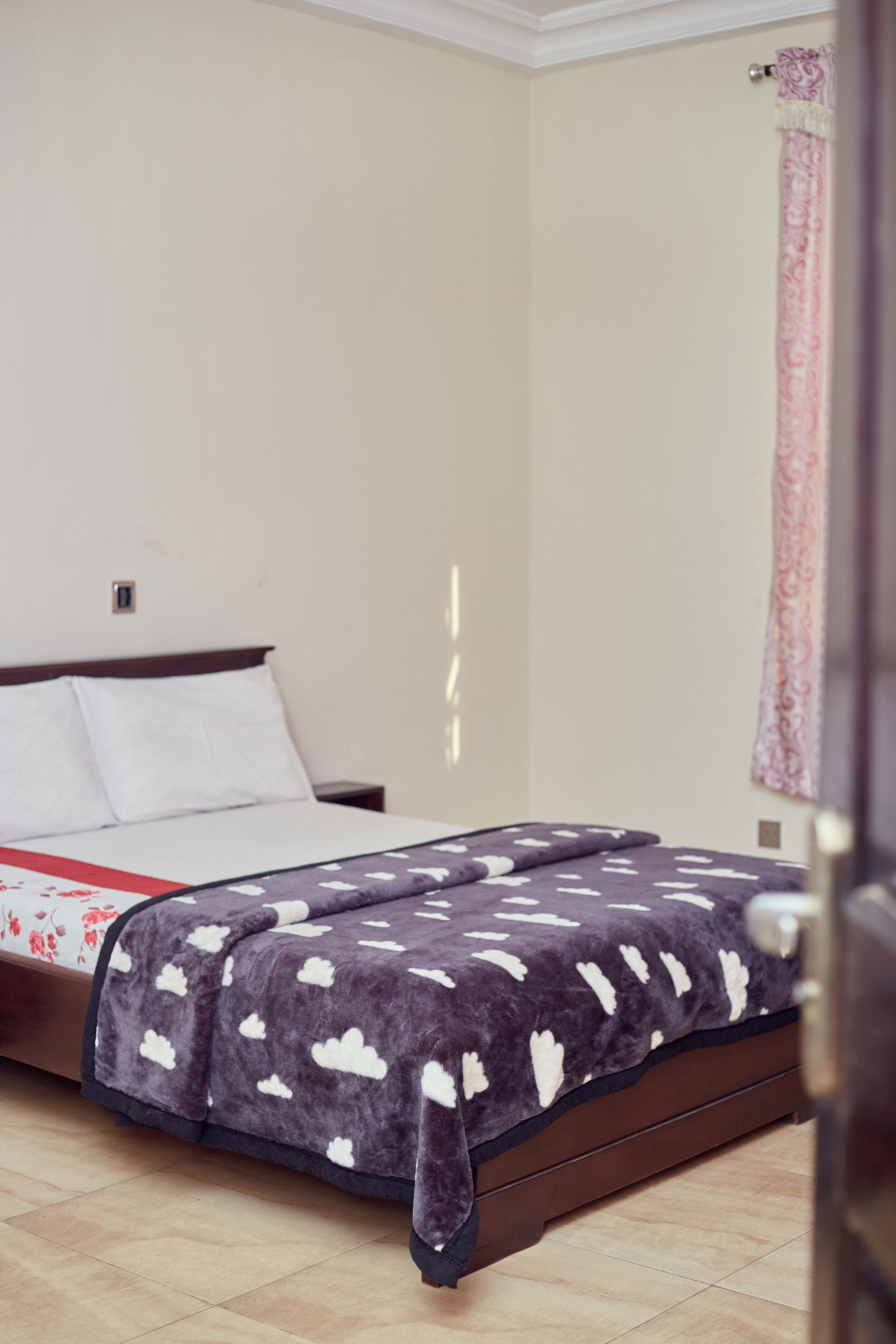 A bedroom with a bed, a nightstand, and a window with curtains.