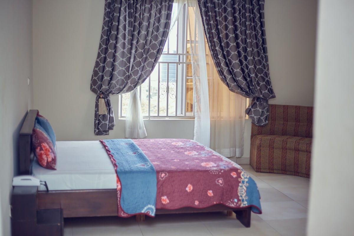 Ein Schlafzimmer mit einem Bett, einem Nachttisch, einem Fenster mit Vorhängen und einem Sofa.