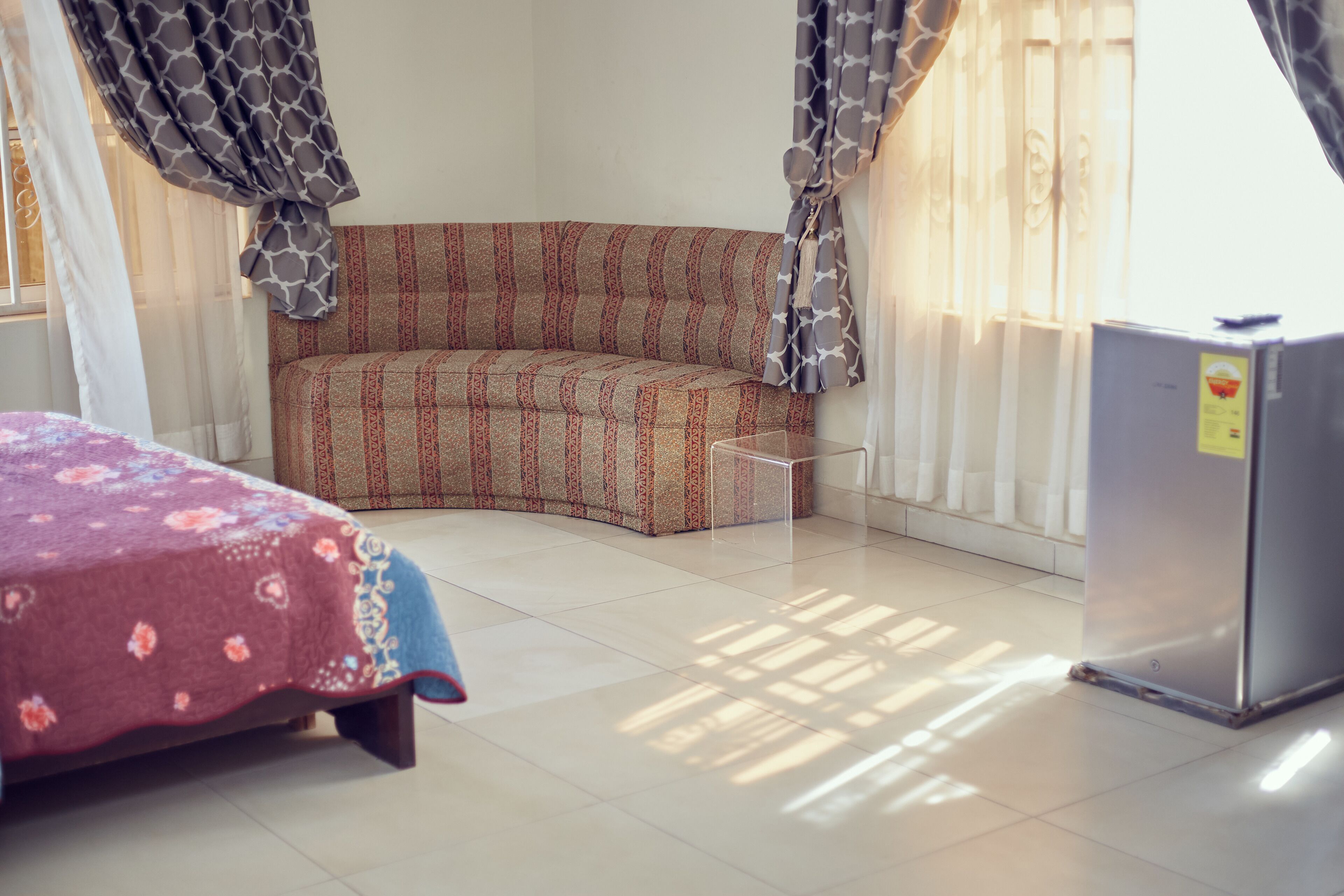A room with a bed, a sofa, a refrigerator, and a window with curtains.