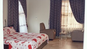 Un dormitorio con cama, dos sillas, una mesita y cortinas.