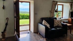 Un salón con un sofá de cuero negro, una mesa de centro de madera y vistas a un paisaje verde a través de una puerta abierta.