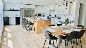 A modern kitchen with white cabinets, a central island with bar stools, and a dining area with a wooden table and chairs.