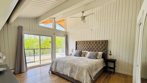 A bedroom with a large bed, a nightstand, a desk, and a sliding glass door leading to an outdoor area.