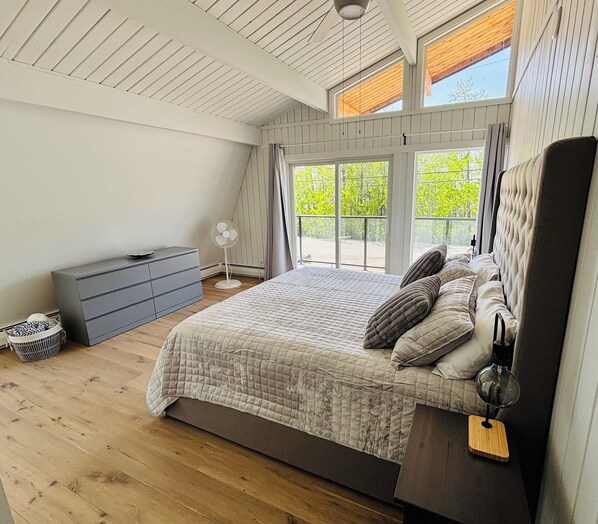 Un dormitorio con una cama grande, un aparador, un ventilador y vistas a zonas verdes por las ventanas.