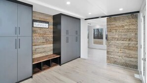 A modern interior with grey cabinets, a wooden bench, and a stone wall.