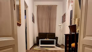 A hallway with wooden flooring, a chandelier, a sofa, and a dining table with chairs.