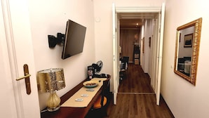 A narrow hallway with a dining table, chairs, a lamp, a television, and a mirror.