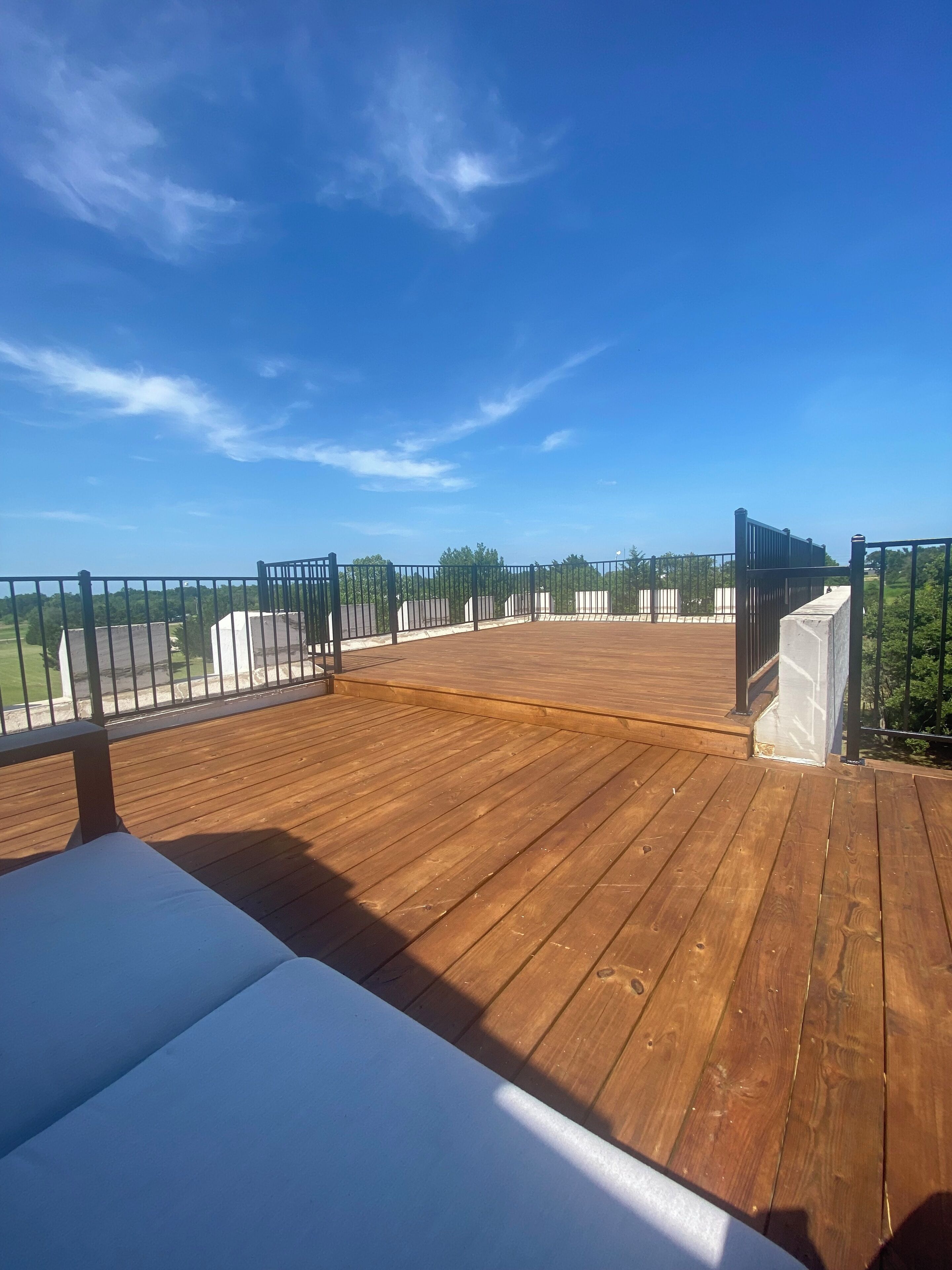 A wooden deck with a clear view of the sky and greenery in the background.