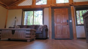 Interior de madera con techo alto, una puerta de madera y una ventana con vistas a un bosque.