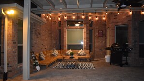 A cozy outdoor seating area with a brick wall, a wooden bench, a patterned rug, and a grill. - Spacious Conroe Home < 4 miles to the Lake! (Montgomery)