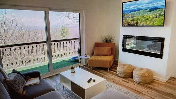A modern living room with a large window, a sofa, a coffee table, and a TV mounted on the wall. - Cozy Elk Hideaway - Walk to Ski Slopes!!! (Beech Mountain)