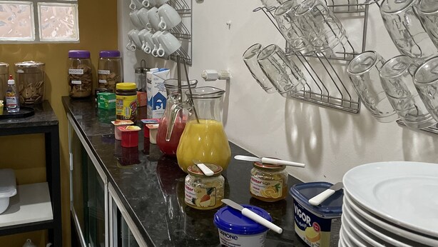 A kitchen with a black countertop, jars of condiments, a yellow pitcher, and a rack of glasses. - Hostel Ipê (São Paulo)