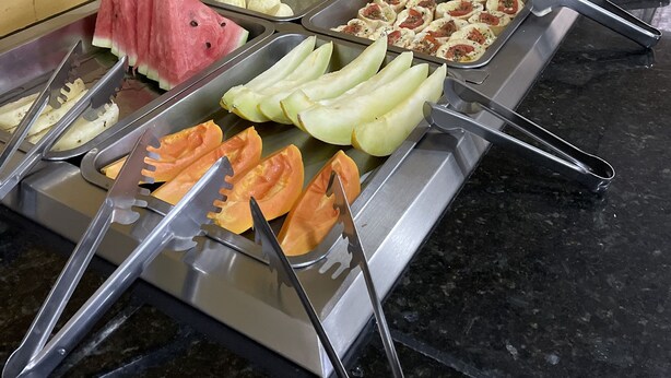 Un bufé con diversos alimentos, entre ellos frutas, pan y pasteles.