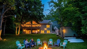 Ein Haus mit Feuerstelle im Garten, umgeben von Stühlen und einer sitzenden Person.