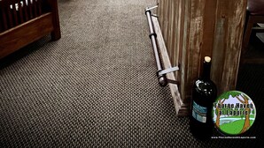 Una sala de estar acogedora con un sofá, una mesa de centro y un televisor. Hay una zona de bar con madera, una botella de vino y un posavasos. Amplias ventanas ofrecen vistas al exterior.