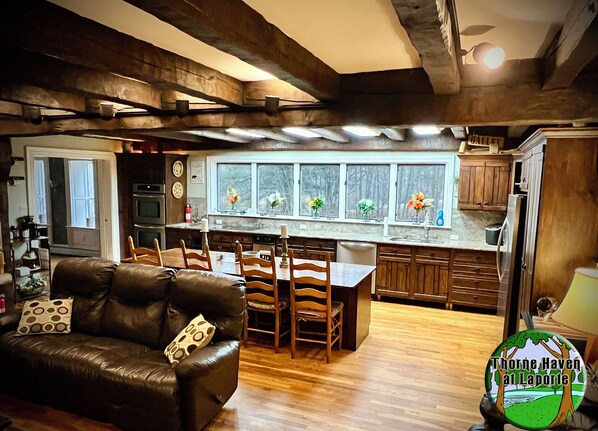 A cozy kitchen with a dining area, wooden cabinets, and a window with flowers.