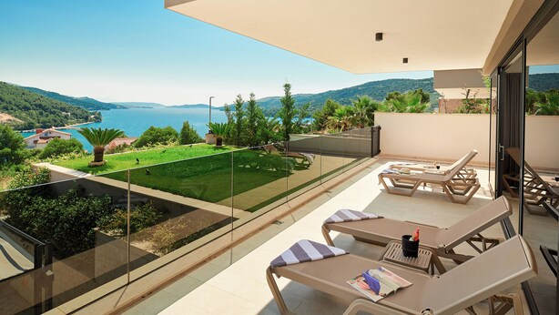 A balcony with sun loungers, a small table, and a glass railing overlooking a scenic view of a lake and hills. - Luxury Villa Cherry with indoor pool and outdoor jacuzzi (Marina)