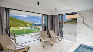 A modern hotel room with a balcony, a pool, and a view of a green landscape. - Luxury Villa Cherry with indoor pool and outdoor jacuzzi (Marina)