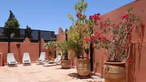 Une cour avec des fauteuils de jardin, de grands pots de plantes et un sol carrelé.