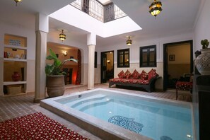 A pool area with a tiled floor, a seating area with red cushions, and a large potted plant. - Private 3-Bedroom Vacation Home in Marrakesh (Marrakech)