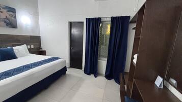 Quarto de hotel com uma cama, janela com cortinas, guarda-roupa de madeira e ar condicionado fixado na parede.