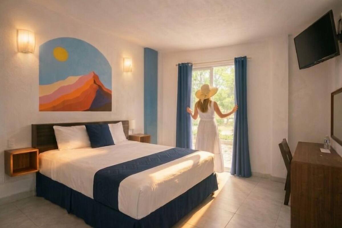 A hotel room with a bed, a desk, a TV, and a painting on the wall.
