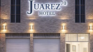 A hotel with a sign reading 'Juarez 70 Hotel,' large garage doors, and a visible entrance with a chair outside. - Hotel Juarez 70 (Colima)
