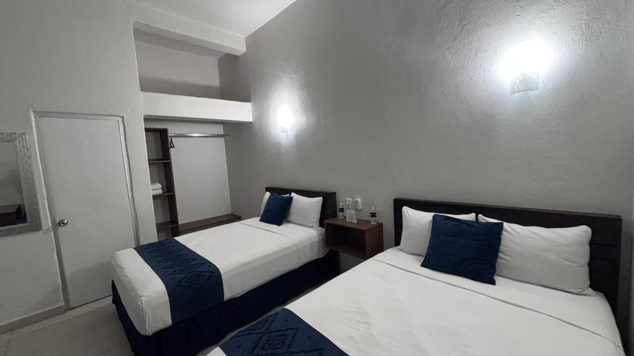Une chambre d’hôtel avec deux lits, une armoire, un miroir et une petite table avec une lampe.