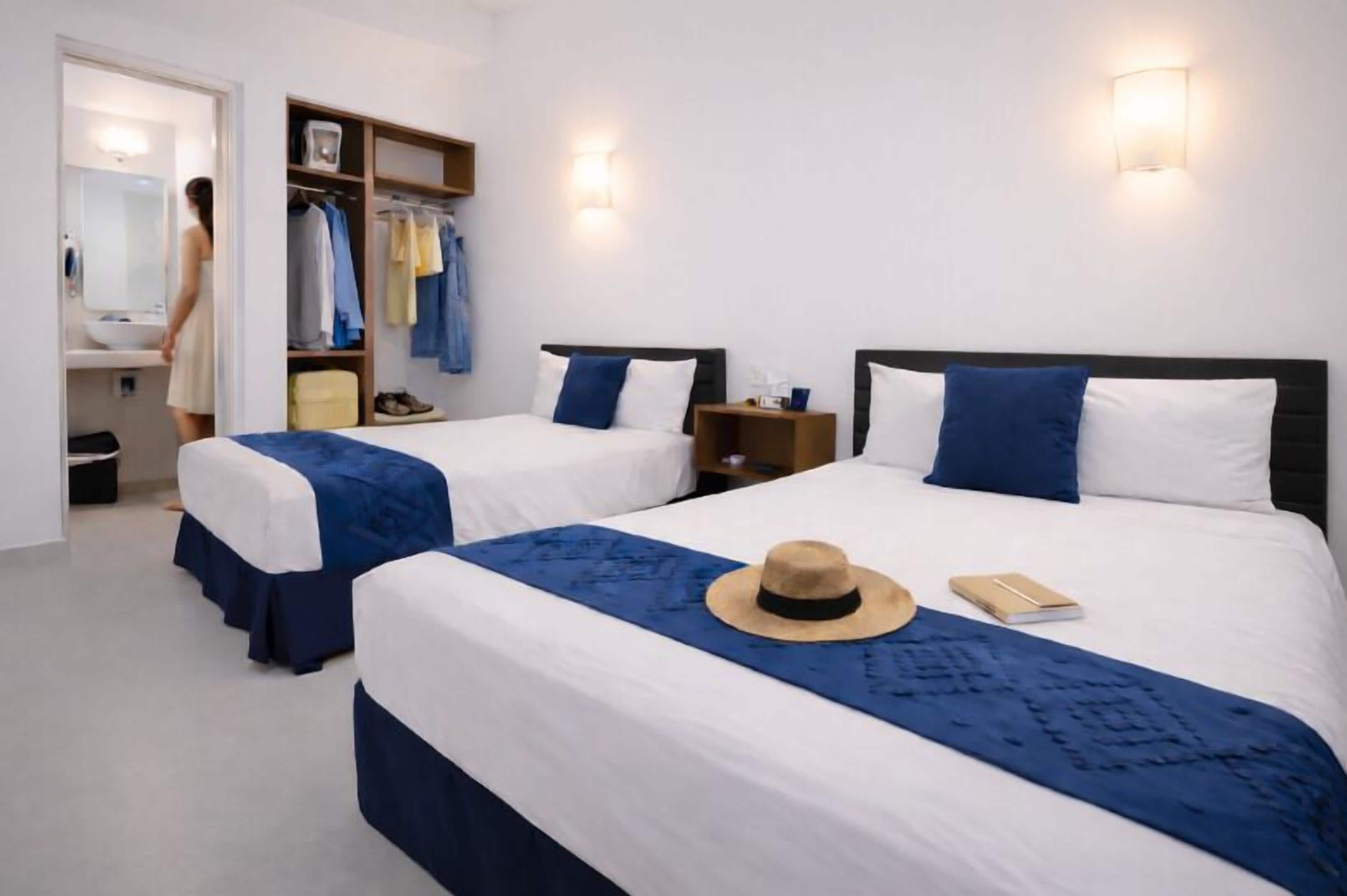 A hotel room with two beds, a wardrobe, a mirror, and a nightstand.