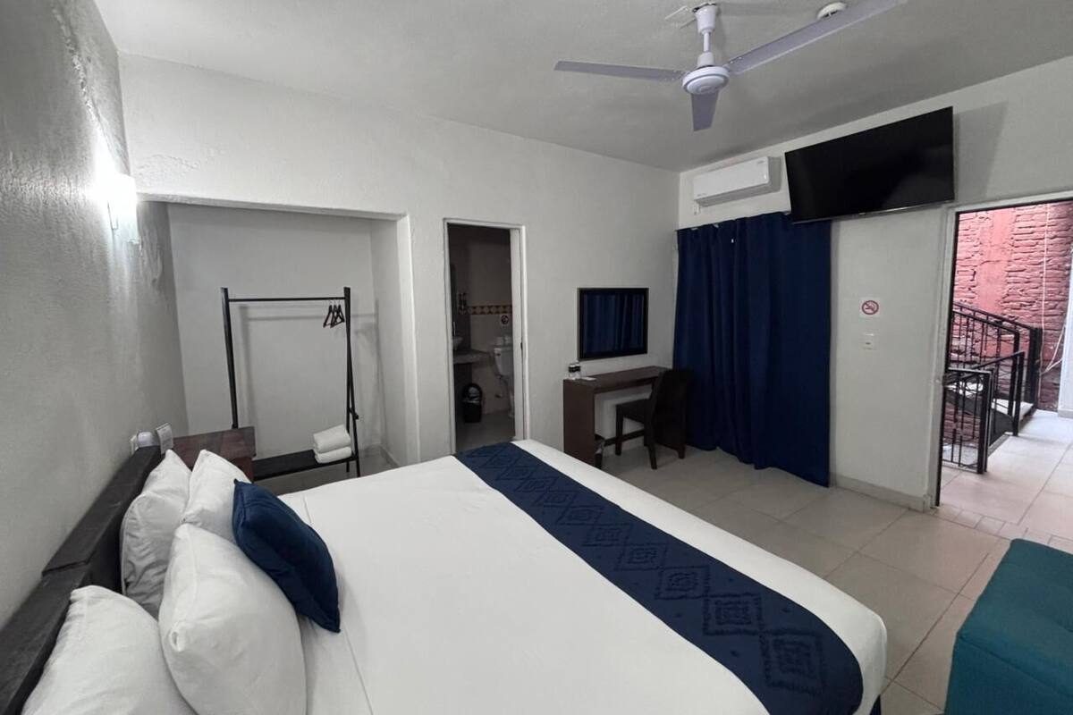 A hotel room with a bed, desk, chair, and a balcony with a view.
