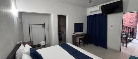 Habitación de hotel con cama, escritorio, silla y balcón con vistas.