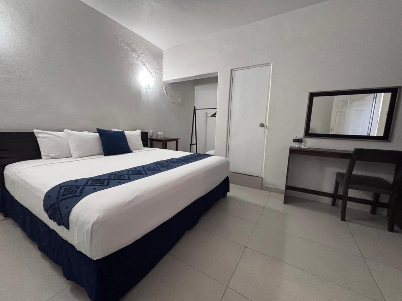 Une chambre d’hôtel avec un grand lit, un bureau, une chaise et un miroir.